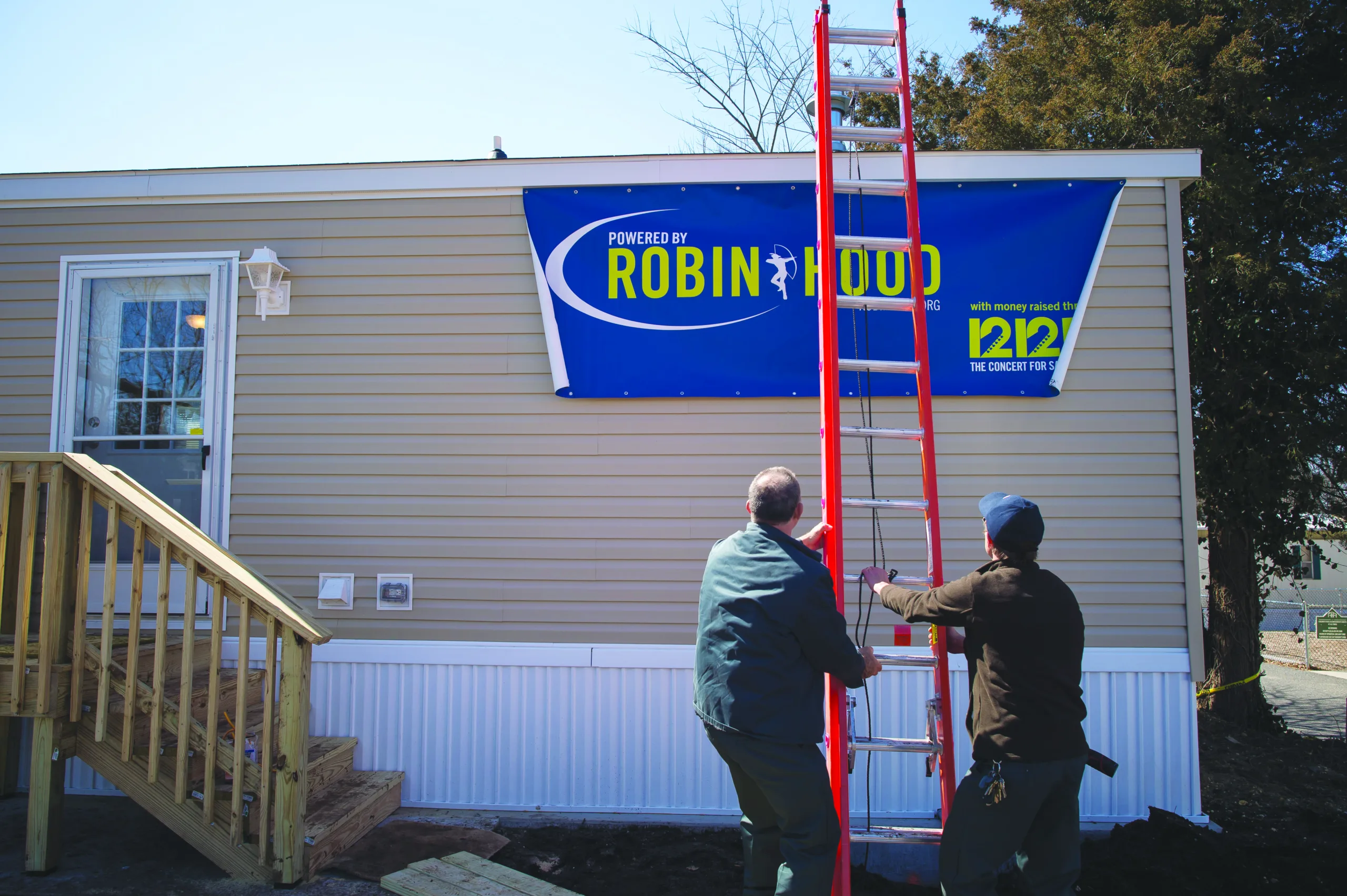 Two men erect a ladder while working on temporary emergency housing.