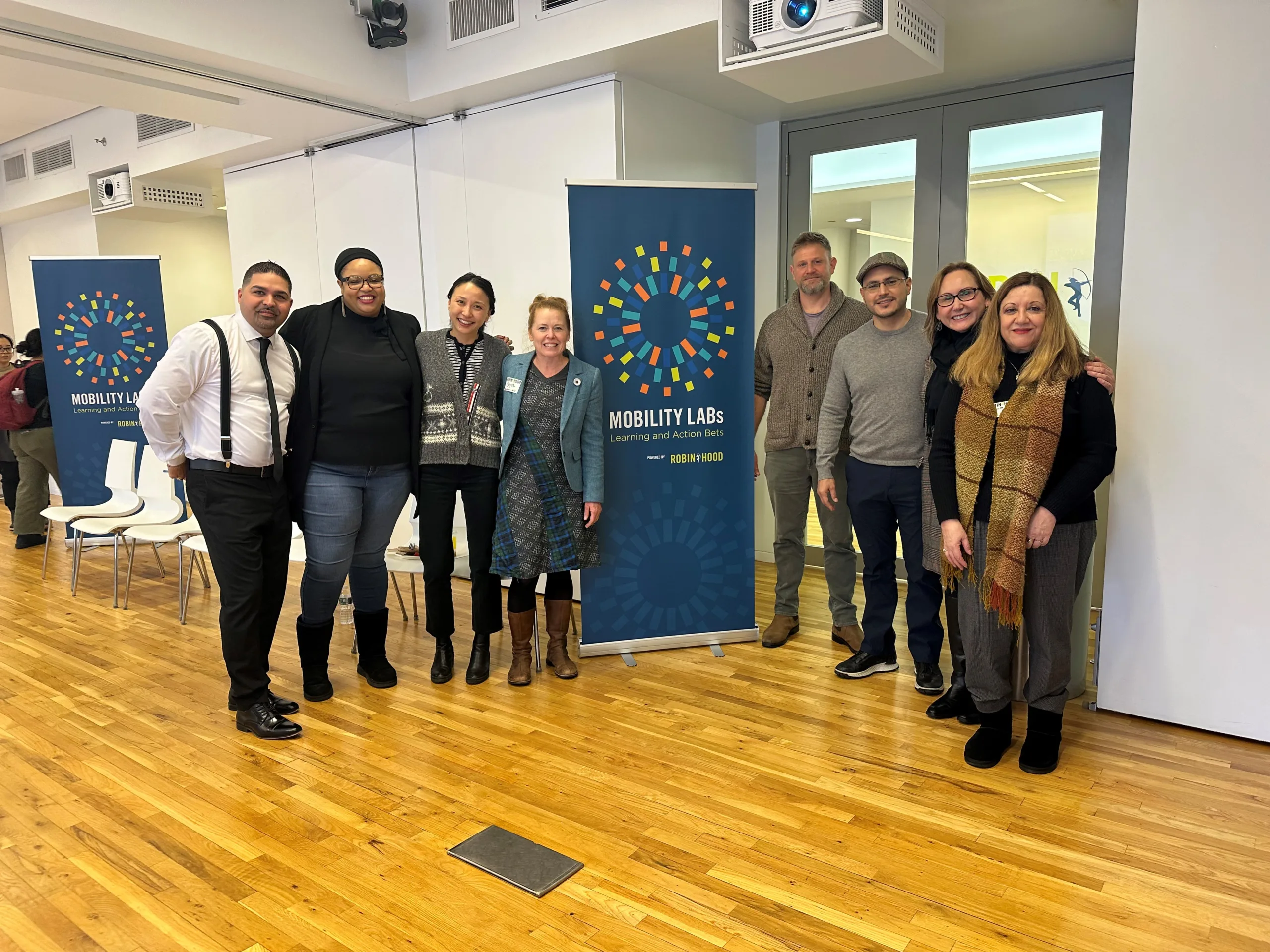 A large group of people posing in an office setting with a pop-up banner between them that reads 
